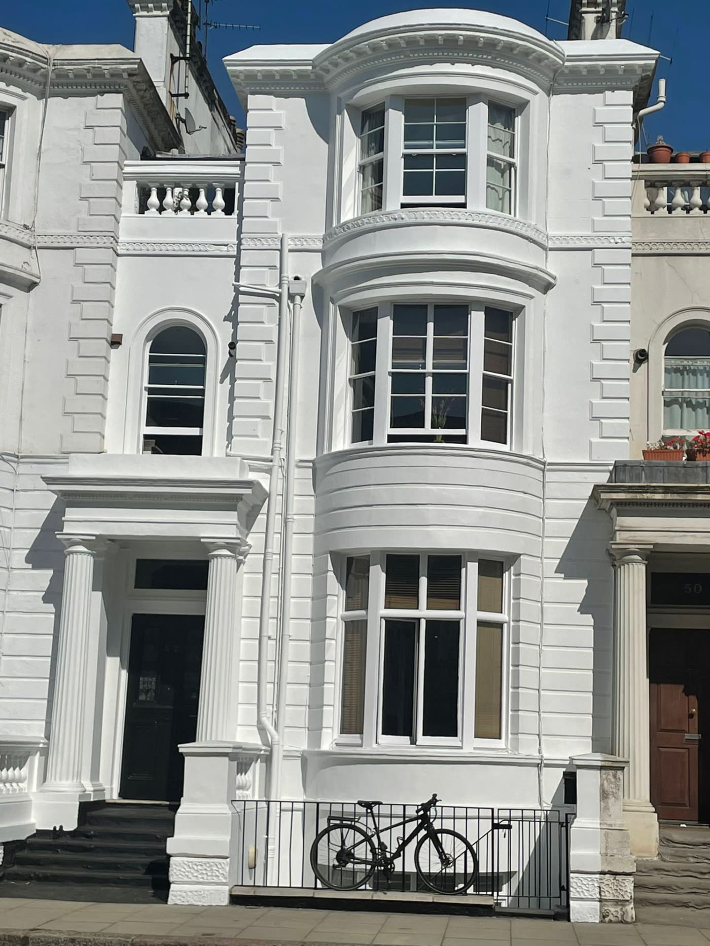 After photo — Kensington period stucco façade repainted in white. Full front elevation of a period terrace — bay windows, columns, quoins and mouldings — repainted in crisp white.